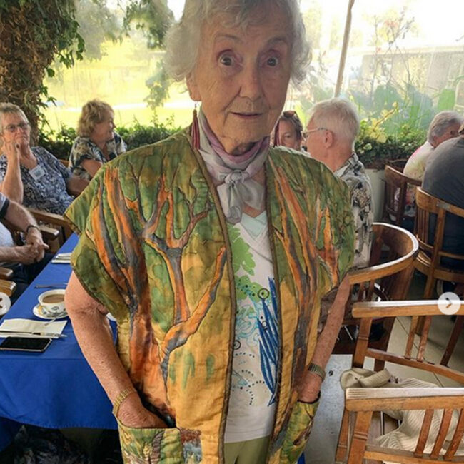 An older woman in a colorful jacket stands at a table during one of the best Queensland tours.