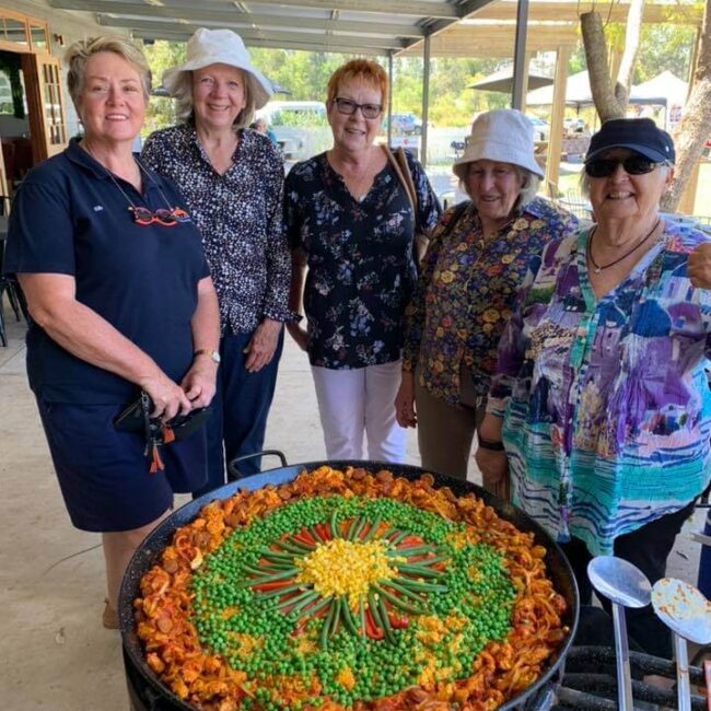 A group of women standing in front of a large pot of food on one of the best queensland tours.