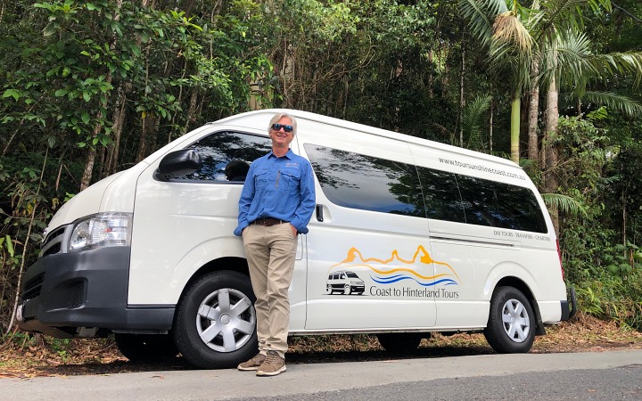 A man standing next to a white van in the Australian forest.